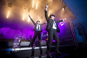 This is a photo of two men perforing a concert as a Blues Brothers tribute duo. They have their hands in the air and are emracingthe atmosphere.