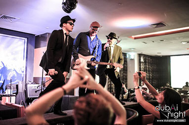 This image shows a Blues Brothers tribute duo in concert with their guitarist iteracting and having fun on stage.