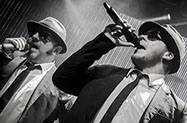 This image shows two men dressed as The Blues Brothers. They are singing.
