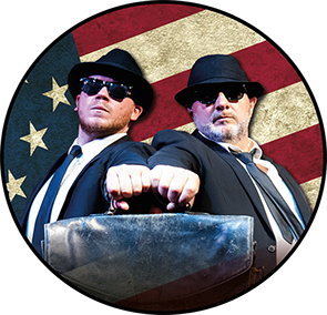 This is a circular image of two men dressed as the Blues Brithers in dark suits, hats and singlasses. They are standing against a US flag.